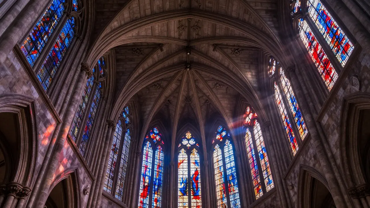 Low angle view of an intricate stone fan vault ceiling with colored light from stained glass.